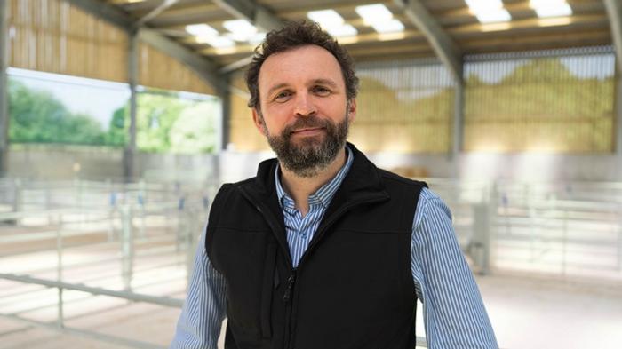 Professor Michael Lee in a short and gilet in a farm building.