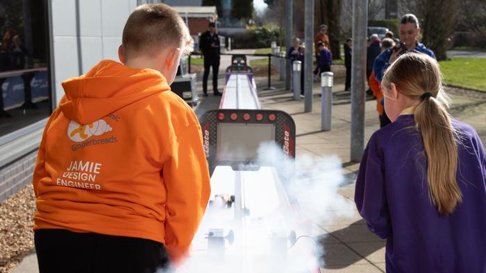 Two school pupils watch a cloud of smoke as a model F1 race car takes off