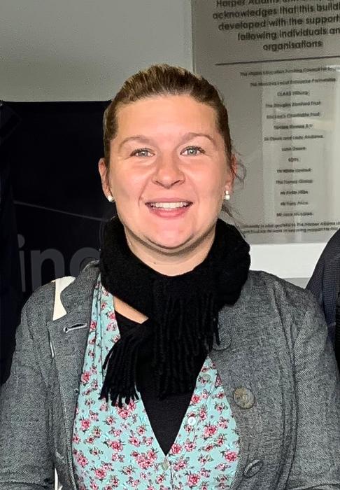 Paula, who wears grey jacket, floral top and black scarf, smiles at the camera