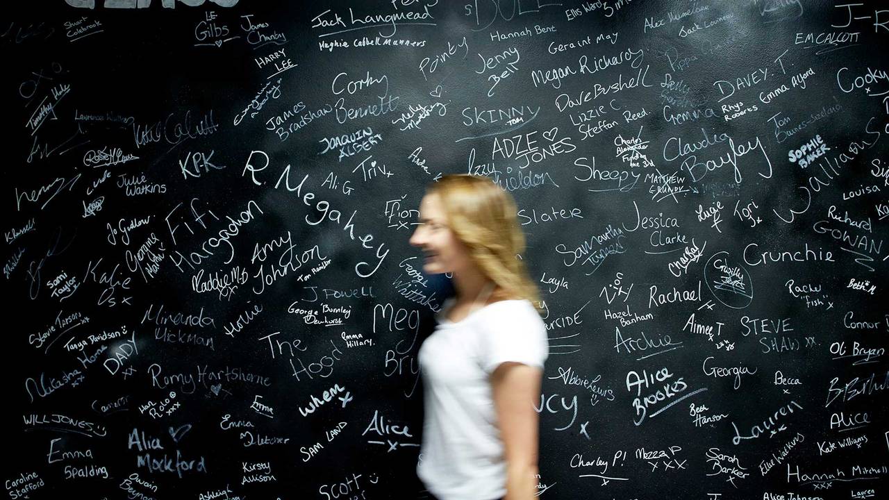 A student walking past a chalk board full of student names